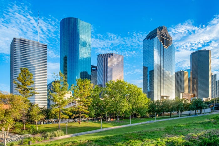 City skyline as seen through cataract-affected vision, showing tall modern skyscrapers with softened outlines, hazy glare, muted colors, and reduced contrast that blur building details and make the bright sky appear diffused.