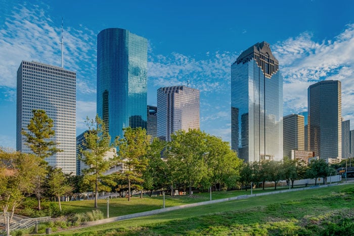 City skyline as seen through cataract-affected vision, showing tall modern skyscrapers with softened outlines, hazy glare, muted colors, and reduced contrast that blur building details and make the bright sky appear diffused.
