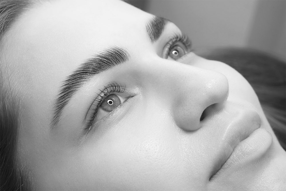 Close-up black-and-white beauty portrait highlighting full brows and long lashes for professional brows and lashes services.