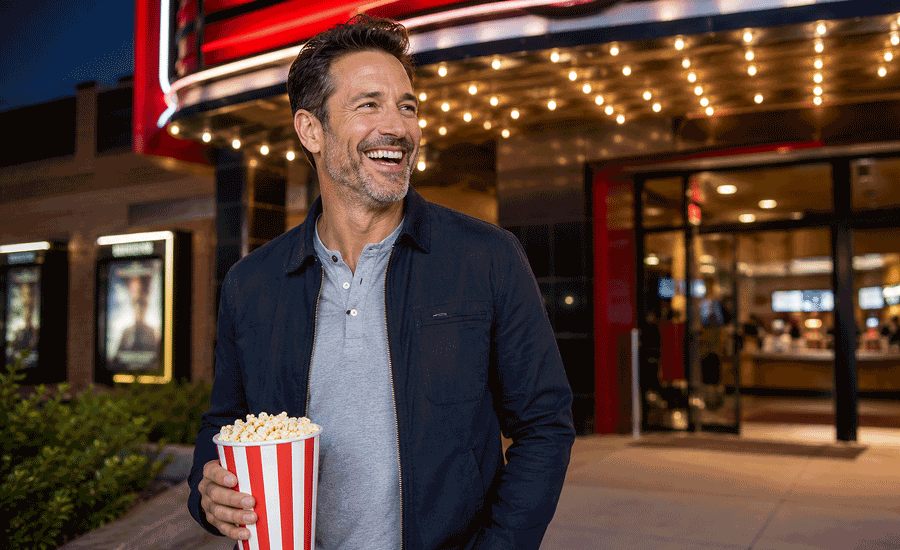 48-year-old man smiling outside a brightly lit movie theater, illustrating eyes sensitive to light for West Texas Eye Associates.