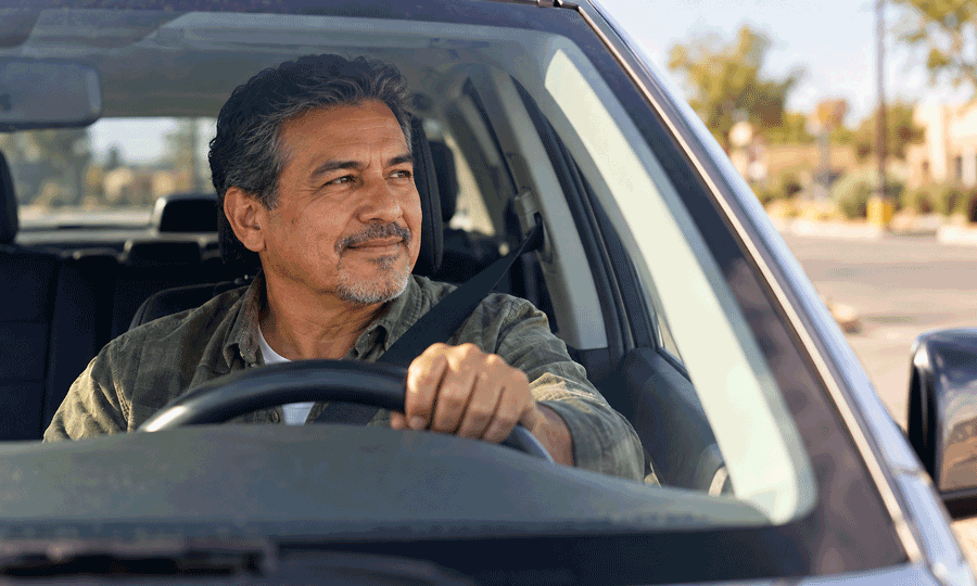 A mature man wearing his seatbelt checks traffic before pulling onto the road, illustrating driving considerations for people with glaucoma.